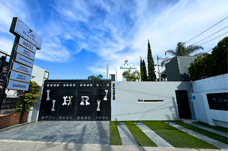 Modern black and white gated driveway entrance to a contemporary building with manicured lawn and directional signage on a sunny day